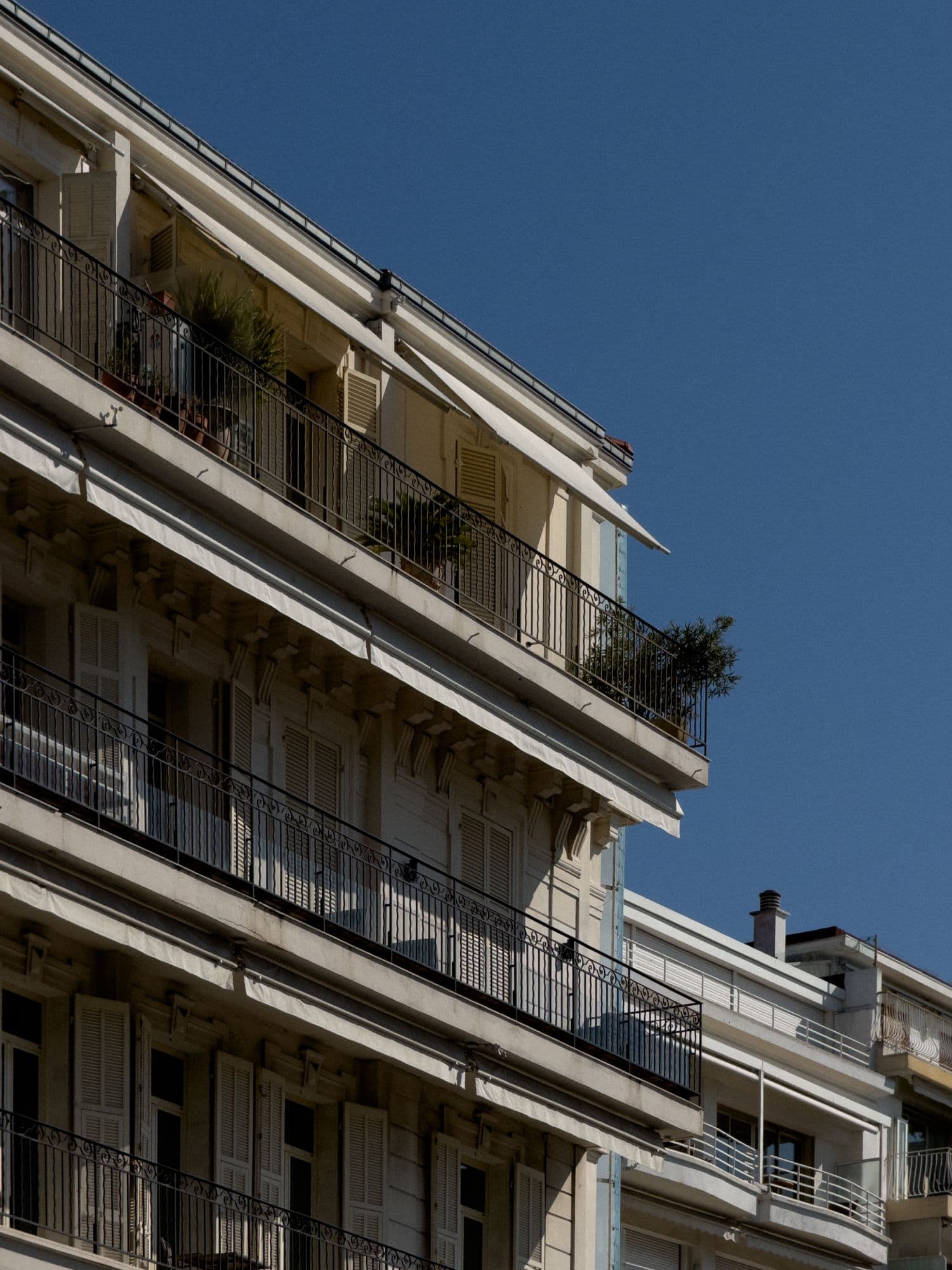 Cream apartment building with wrought-iron balconies against a clear sky, straight from the iPhone