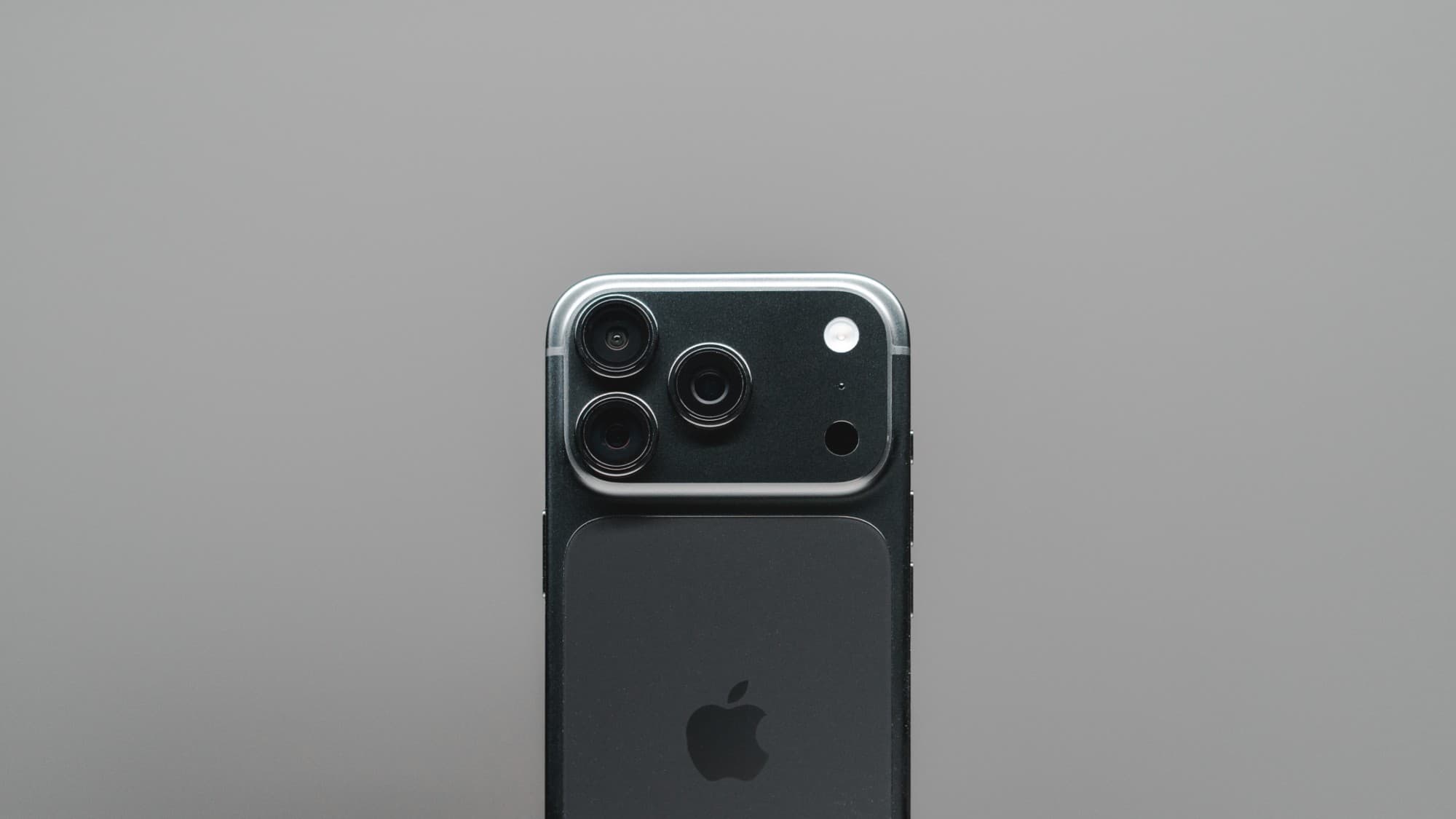 Back of a black iPhone Pro showing its three cameras, against a plain grey backdrop